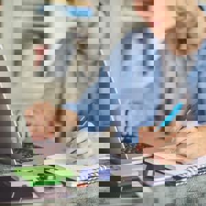 Person on laptop making notes on notepad